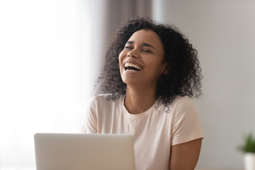 Happy African American woman laughing at funny joke, using laptop