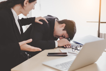 Fototapeta premium Businessman or colleagues guy sleeping during working with businesswoman. Workmate woman trying to wake up him but he still sleeping on desk at office. She get frustrated, unhappy, angry with lazy guy