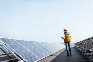 View on the rooftop solar power plant with mann walking and examining photovoltaic panels. Concept of alternative energy and its service © rh2010