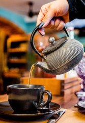 metal teapot pour black tea in black glass mug in cafe