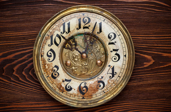 Old clock with a rusty clock face on wooden background.