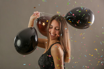 Attractive woman holding black baloons and dancing under falling confetti, party and holiday season...
