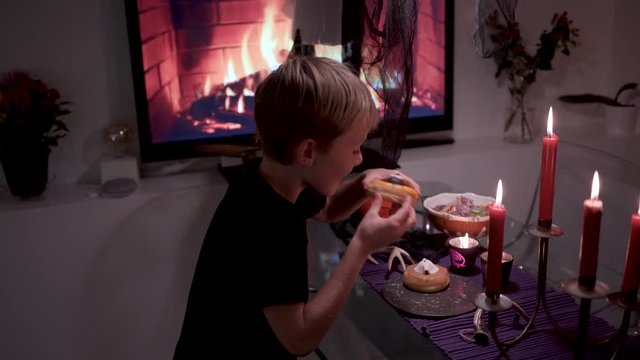A boy trying to steal Halloween donut from decorated table dark moody style with scary accessories rack focusing camera