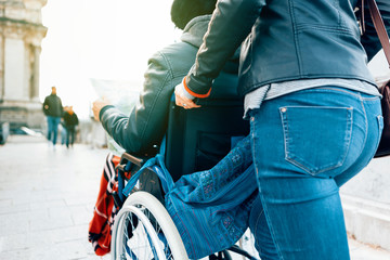 Obraz premium side view of a man sitting in a wheelchair holding a map in his hands while a female person in casual clothing is pushing him around the city