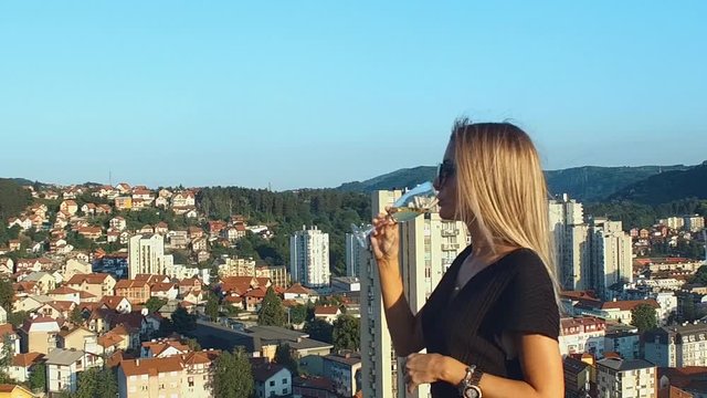 Young caucasian blonde woman sipping wine on roof top, slow motion