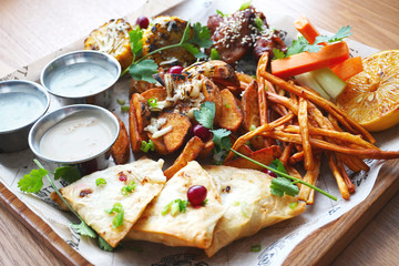 a plate of beer snacks. Corn with cheese, smoked cheese, chicken wings, potato slices with cheese, envelopes with meat vegetables, herbs and three sauces.