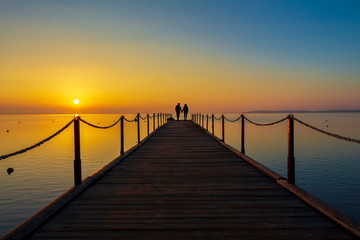 Fototapeta na wymiar couple in love meets the dawn on the pier. sunrise over the water. Silhouettes of man and woman. romantic morning
