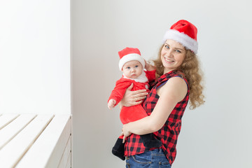 Obraz premium Family, childhood and Christmas concept - Young mother holding baby in santa suit indoor