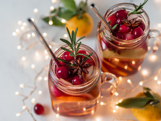 Winter sangria in mason jars with metal straws on christmas holiday background. Decorated fruit slice, cranberry and rosemary. Copy space for text or design. Horizontal. Decoration lighting chain
