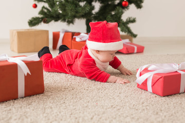 Cute baby girl wearing santa claus suit crawling on floor over Christmas tree. Holiday season.