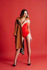 Fashion portrait of young woman in jacket and red swimsuit. Pink background, studio shot