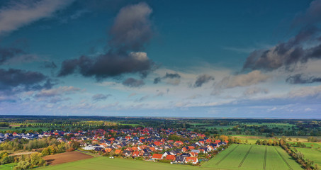 Aerial view of a village between agricultural areas, with a high blue sky and a dramatic cloud.