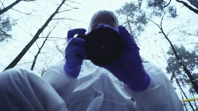 Crime investigator in safety uniform taking photo of victim under body bag