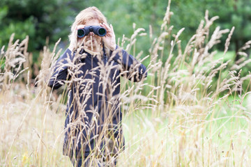 Mature woman hidden in the bushes watching forest wildlife with binoculars, copyspace