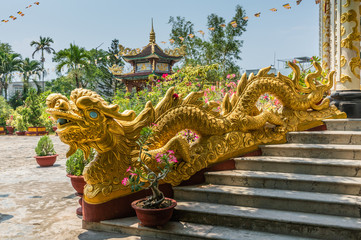 Nha Trang, Vietnam - March 11, 2019: Chua Loc Tho Buddhist temple, primary school and orphanage. Large and long Golden dragon statue as border of stairway to temple under blue sky with green foliage.