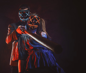 Crazy couple in spooky masks are posing for photographer with baseball bat.