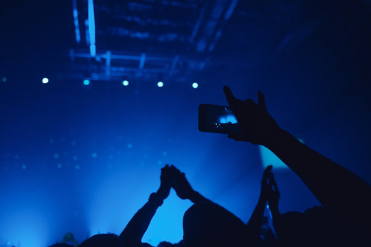 People taking photographs with smart phone during a music concert. Hands with gesture Horns. That rocks.  Person capturing a video on a mobile phone at a music festival.