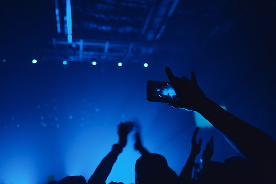 People taking photographs with smart phone during a music concert. Hands with gesture Horns. That rocks.  Person capturing a video on a mobile phone at a music festival.