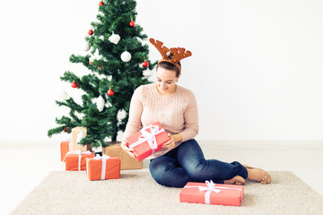 christmas, x-mas, winter, happiness concept - girl opens a gift against the background of the Christmas tree. Happy young woman celebrating Christmas