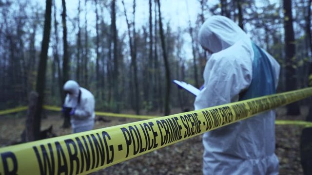 Forensic analysts working at crime scene secured by tape, evidence collection