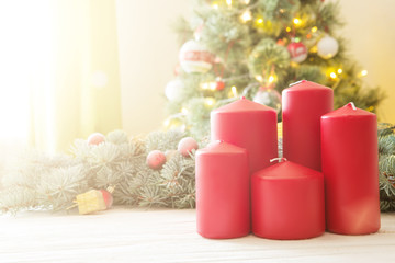 Red christmas candles on white wooden plank against christmas tree in living room