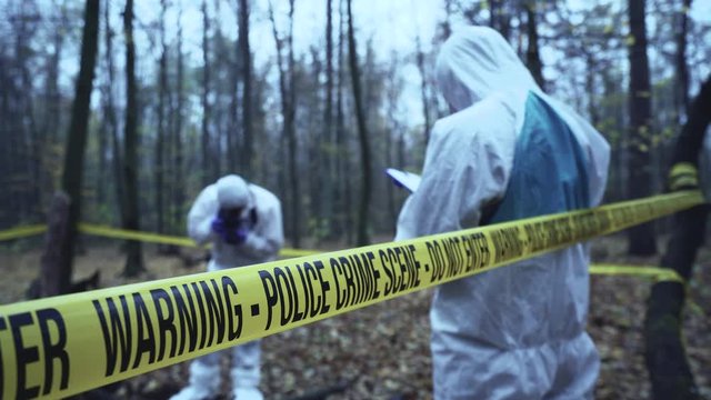 Police experts working at crime scene in forest, murder investigation, forensics