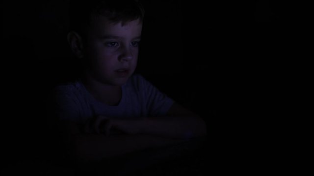 Little boy looking at the notebook display in the night. Child use laptop and watching video