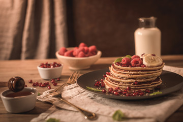 Pancakes with raspberries, banana slices, pomegranate seeds and honey