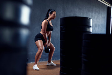 Fototapeta na wymiar Woman fitness model make workout with weights - squat with kettlebell. Tanned sporty female, with black hair. Gym lifestyle.