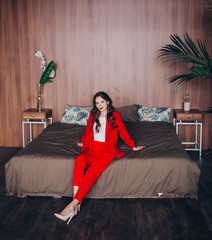 elegant lady in a red suit sitting on a bed in a hotel