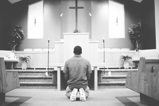 Grayscale of a male on his knees praying in the church with a blurred background