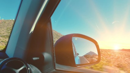 Peak of a volcano mountain reflected in the rear view mirror of a car while driving. The rays of the sunset shine into the camera. The concept of travel, promotion to your goal, success.