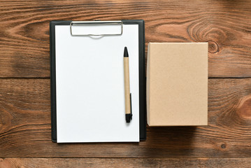 Postal cardboard box and blank page document with a pen on the brown table background.