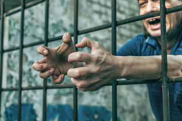 A depressed man holds his hands on the prison bars. Prisoner for the crime. Poor conditions....