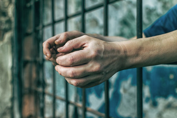 A depressed man holds his hands on the prison bars. Prisoner for the crime. Poor conditions. Scream, despair, pain, hunger.