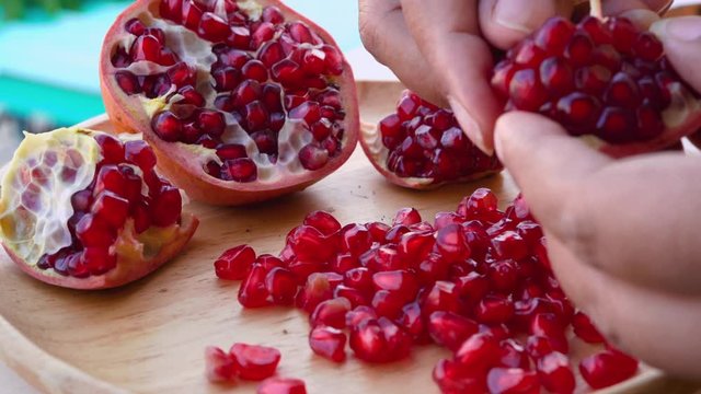 Chef is peeling pomegranate seeds on a wooden plate to eat.