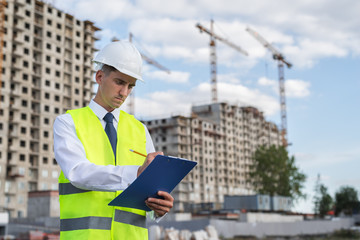 civil engineer in a white helmet makes pencil marks in the documentation.