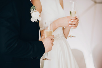 Stylish wedding couple holding champagne glasses and toasting at wedding reception in restaurant,...
