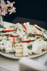 Goat cheese, red peppers and greenery appetizers on table at wedding or christmas feast. Luxury catering concept. Delicious italian food table at wedding reception.