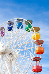 Ferris wheel with white structure and colored cabins on background of blue sky