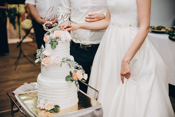 Bride and groom cutting stylish wedding cake at wedding reception in restaurant. Wedding couple...