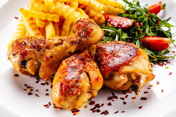 Roast chicken drumsticks with french fries and vegetables on white background