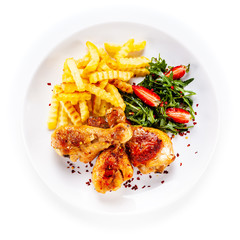 Roast chicken drumsticks with french fries and vegetables on white background