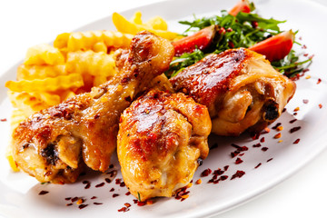 Roast chicken drumsticks with french fries and vegetables on white background