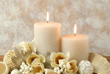 Fototapeta na wymiar Spa concept of burning cream colored candles arranged with natural potpourri elements and flowers on a warm background