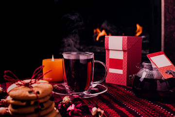 Hot tea or coffee in a red mug, ginger cookies on vintage wood table. Fireplace as background. Christmas or winter warming drink. Layout with free text space.