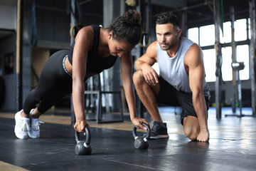 Obraz na płótnie Canvas Sporty woman doing push-up in a gym, her boyfriend is watching her.