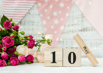 May 10 date on a wooden calendar, roses, holiday flags and a garland on a white background. Mother's day concept