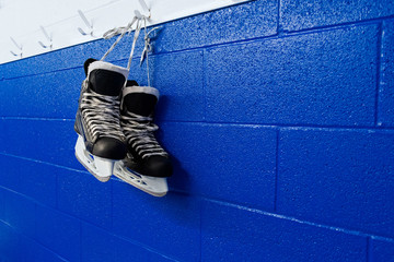 Hockey skates hanging in locker room over blue background with copy space 