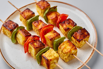 Paneer Tikka at skewers in white plate isolated at white background. Paneer tikka is an indian cuisine dish with grilled paneer cheese with vegetables and spices. Indian food.